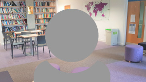 A grey person icon showing just head and shoulders with a teaching space with table chairs and bookcase background.